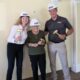Three individuals wearing construction hard hats and holding ceremonial golden hammers during a preservation project kickoff event inside a historic building.